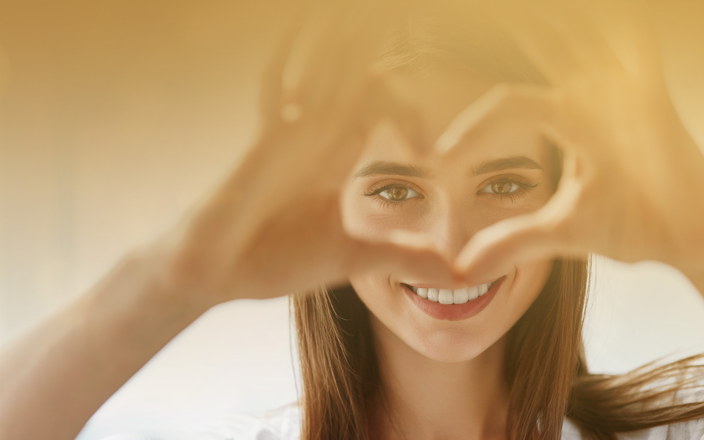 Lächelnde Frau, die mit ihren Händen ein Herz um ihre Augen formt.